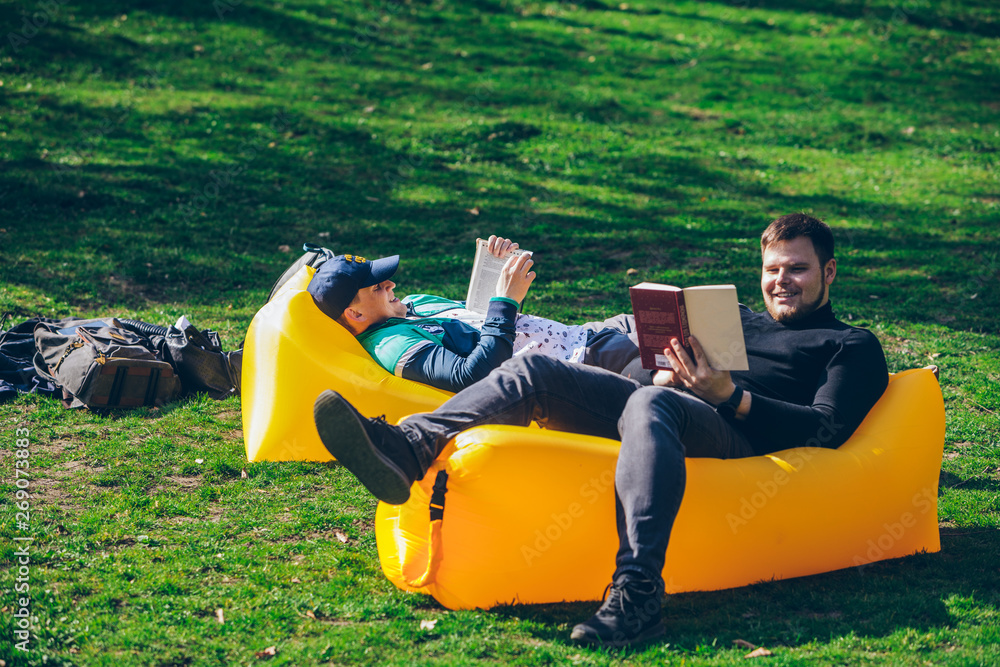 two men friends laying on yellow inflatable mattress reading books