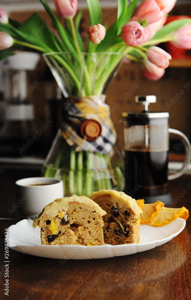 Muffins cakes with candied fruit and zest on white plate. French press coffee. Pink tulips in decanter Muffins cakes with candied fruit and zest on white plate. French press coffee. Pink tulips in decanter