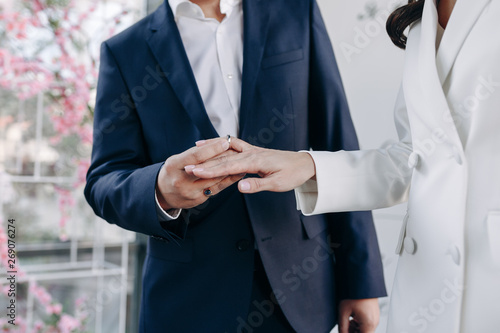Picture of Man Putting Engagement Silver Ring on Women Hand. Close-up of Couple Exchanging Love Symbol during Wedding Ceremony Outdoor. Happy Married People Romantic Flower Background