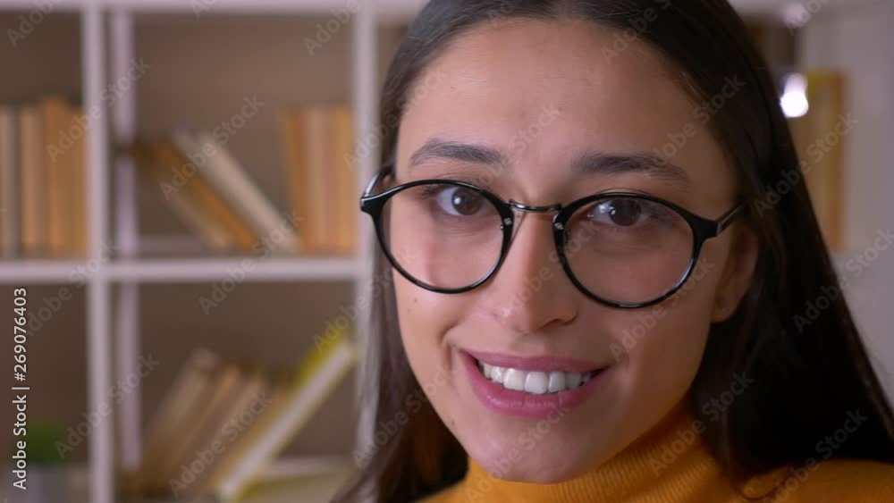 Close-up portrait of stylish brunette teacher in glasses smiles happily into camera at the library. Close-up portrait of stylish brunette teacher in glasses smiles happily into camera at the library.