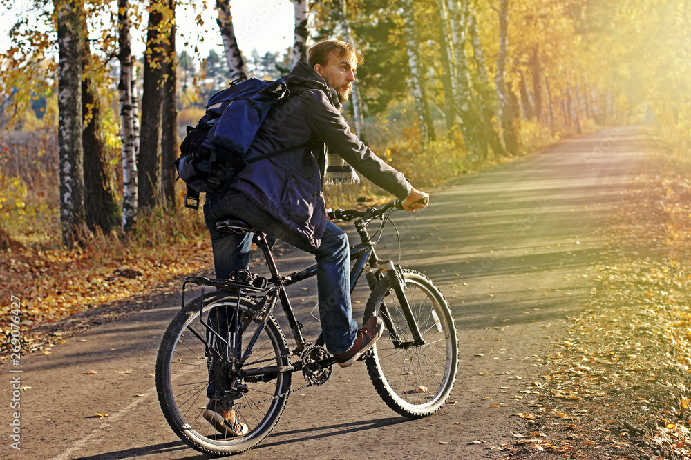 Bearded hipster man in casual wear with backpack and bicycle in autumn park or forest on sunset. Discovery beautiful fall season