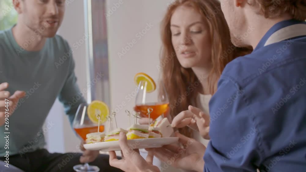 Four friends happy talking, eating and drinking cocktail appetizers.Happy people group enjoy modern home party dinner or lunch.Handheld video Four friends happy talking, eating and drinking cocktail appetizers.Happy people group enjoy modern home party dinner or lunch.Handheld video