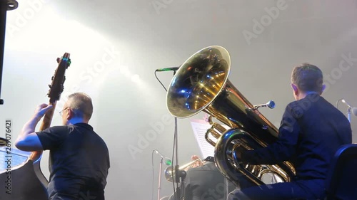 Symphony orchestra on the stage, orchestral brass section, behind the scenes shoot.Tubaist in black shirt blow in big brass tube. photo