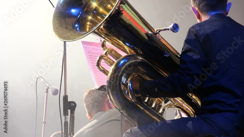 Tubaist in an orchestra on the stage, holds big brass tube, behind the scenes shoot. Close up, smoke moves around scene photo