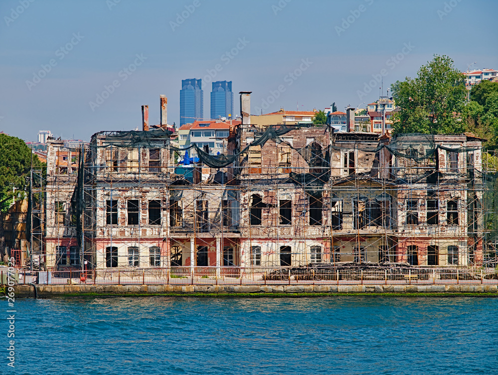 Bosporus strait, view from cruise ship. Old traditional damaged wooden building with structural support and TAT twin towers at the background.