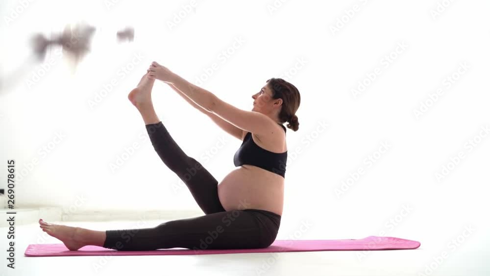 Pregnant brunette girl doing yoga on a white background. Authentic style with natural light and shadows.