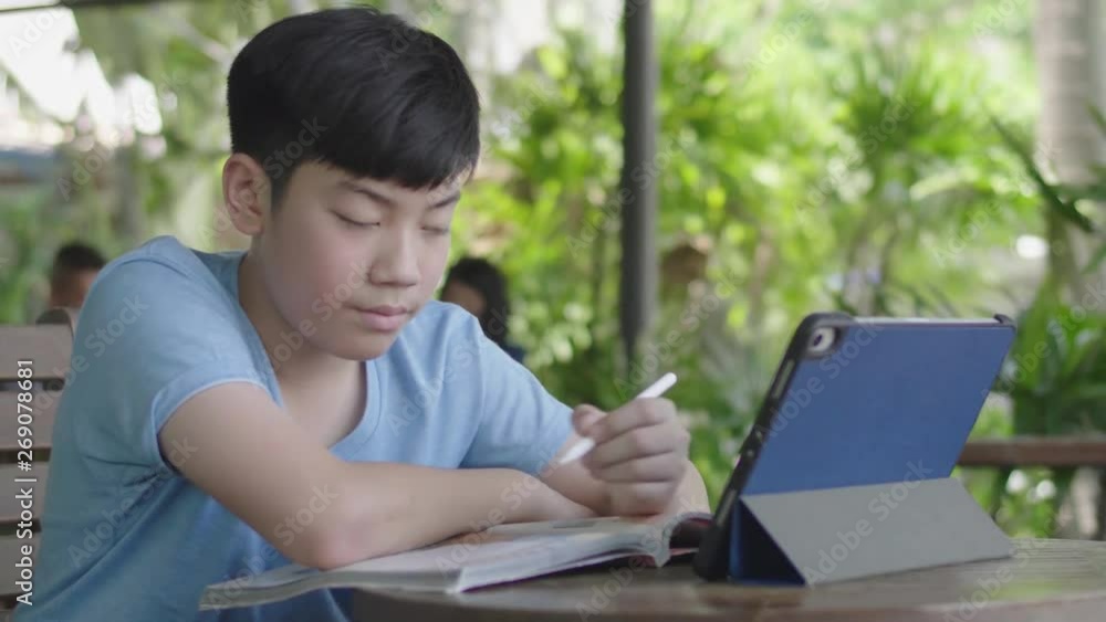 Cute asian boy using tablet computer ,Young teenage boy doing homework on digital tablet with silently face . Cute asian boy using tablet computer ,Young teenage boy doing homework on digital tablet with silently face .