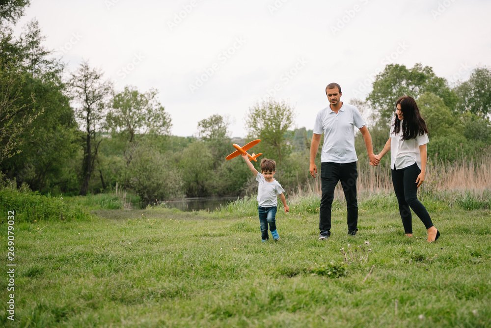 Fototapeta premium Father, mother and son playing with toy airplane in the park. friendly family. People having fun outdoors. Picture made on the background of the park and blue sky. concept of a happy family.