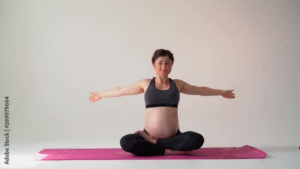 Pregnant brunette girl doing yoga on a white background. Authentic style with natural light and shadows. Pregnant brunette girl doing yoga on a white background. Authentic style with natural light and shadows.