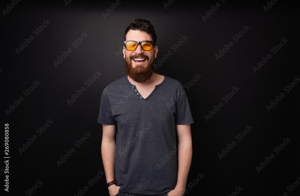 Photo of bearded guy wearing stylish sunglasses, smiling at camera over dark background