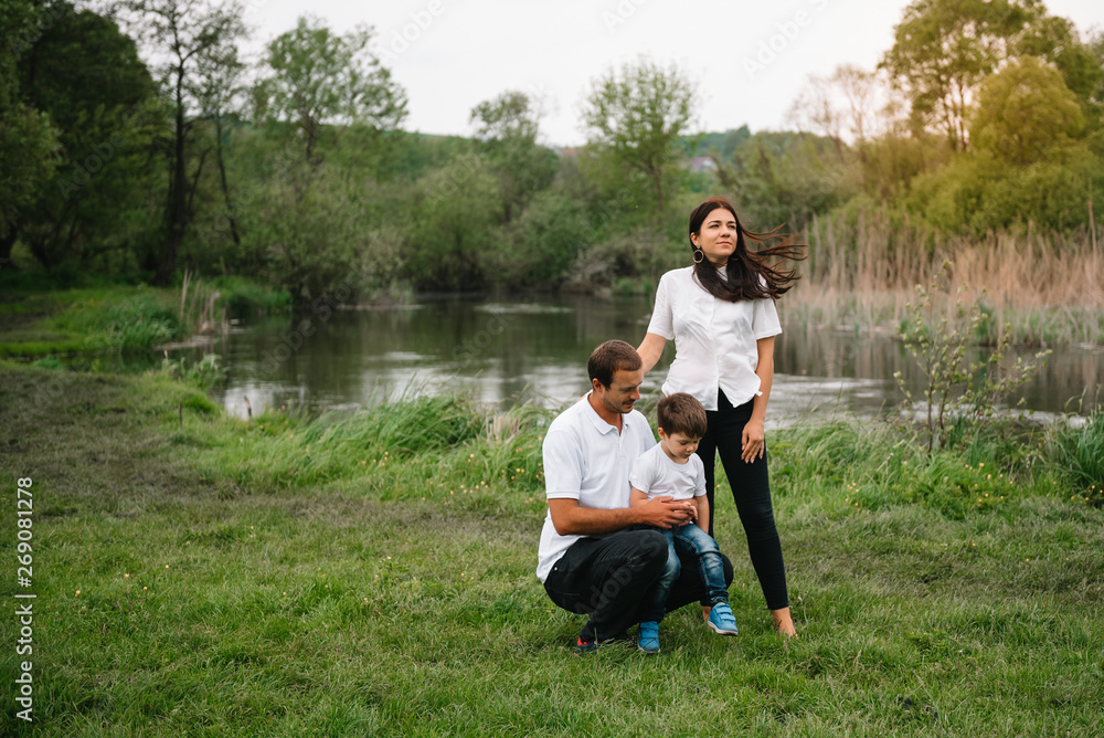 Fototapeta premium Happy family: mother father and child son on nature on sunset. Mom, Dad and kid laughing and hugging, enjoying nature outside. Sunny day, good mood. concept of a happy family