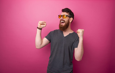 Photo of winner bearded guy celebrating with rised hands over pink background