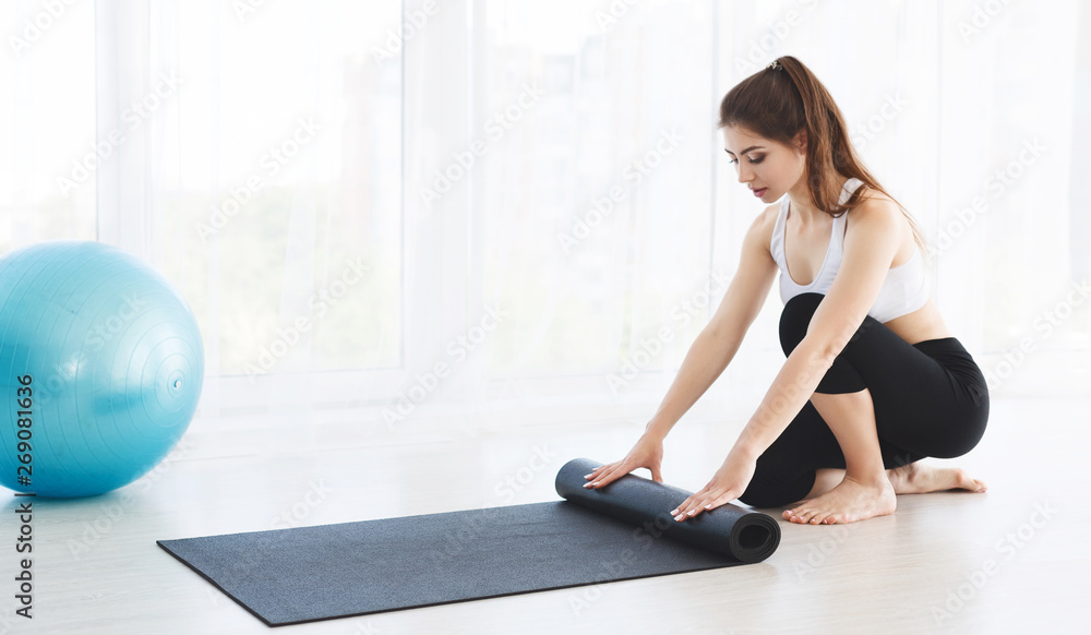 Young yoga woman rolling her mat after training