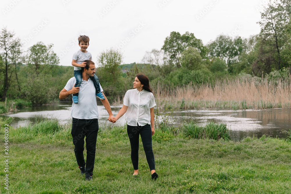 Fototapeta premium Happy family: mother father and child son on nature on sunset. Mom, Dad and kid laughing and hugging, enjoying nature outside. Sunny day, good mood. concept of a happy family