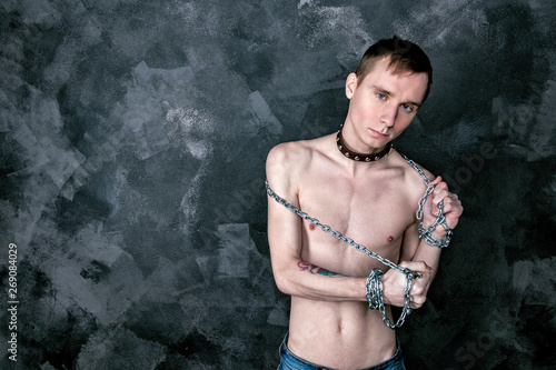 Handsome skinny guy in collar holding a chain. Black background