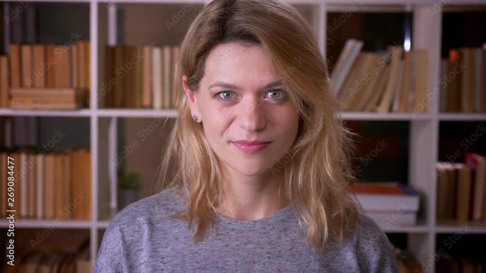 Cute middle-aged blonde teacher laughing joyfully into camera being happy at the library. Cute middle-aged blonde teacher laughing joyfully into camera being happy at the library.