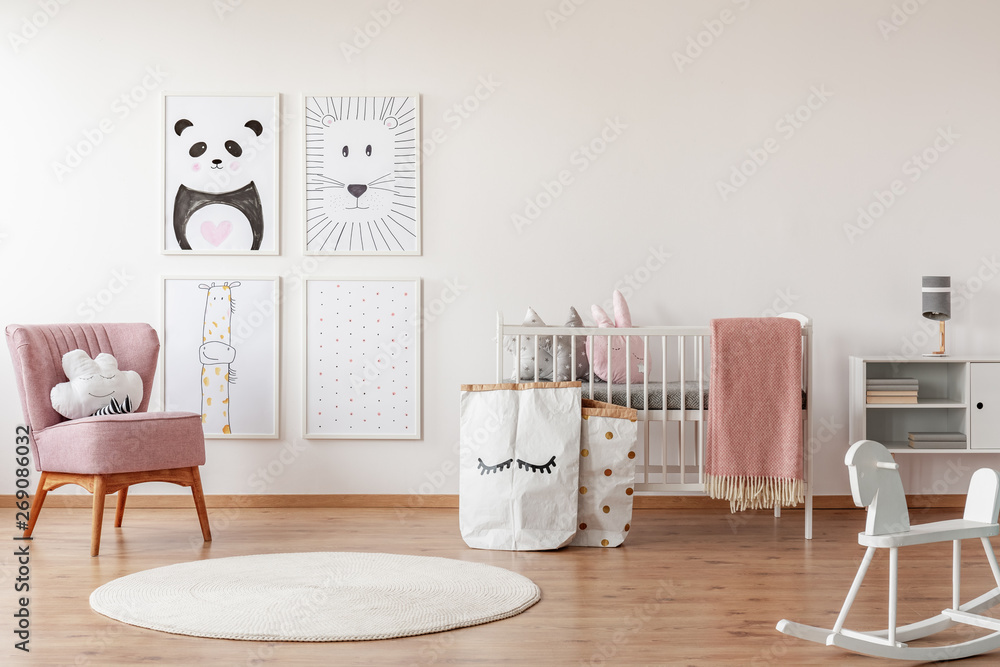 Fototapeta premium Rocking horse and pink chair in child's room interior with posters, white rug and cradle. Real photo