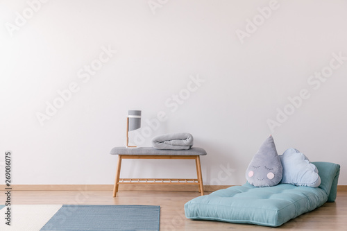 Pillows on blue mattress next to bench with lamp in white simple kid's bedroom interior. Real photo