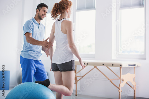 Physiotherapist supporting woman during rehabilitation with ball