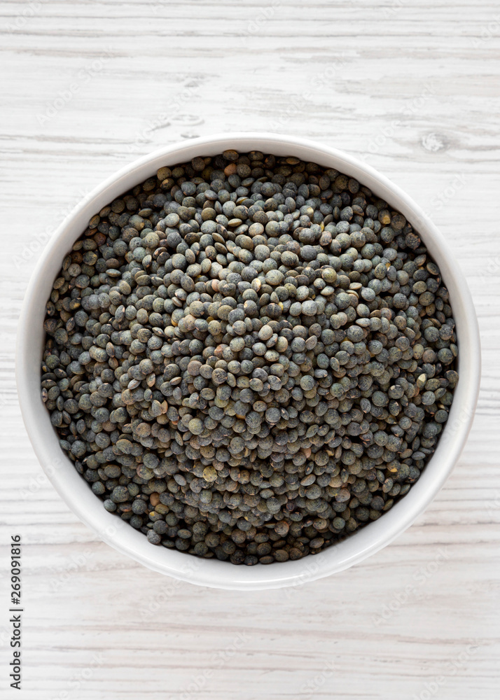 Dry green french lentils in a bowl over white wooden surface, top view. Flat lay, overhead, from above. Close-up. Dry green french lentils in a bowl over white wooden surface, top view. Flat lay, overhead, from above. Close-up.