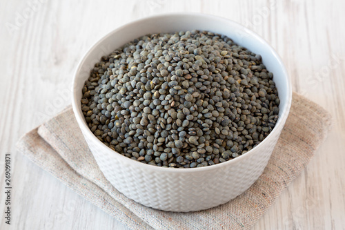 Dry green french lentils in a bowl over white wooden background, side view.