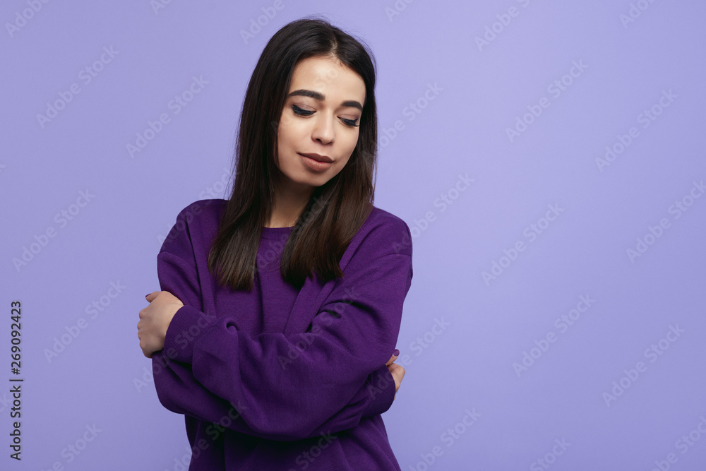 Stylish young girl with closed eyes, wearing purple sweater, holding arms crossed while standing isolated over violet background Stylish young girl with closed eyes, wearing purple sweater, holding arms crossed while standing isolated over violet background