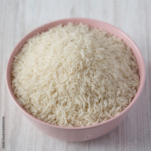 Dry white rice basmati in a pink bowl over white wooden surface, side view. Close-up.