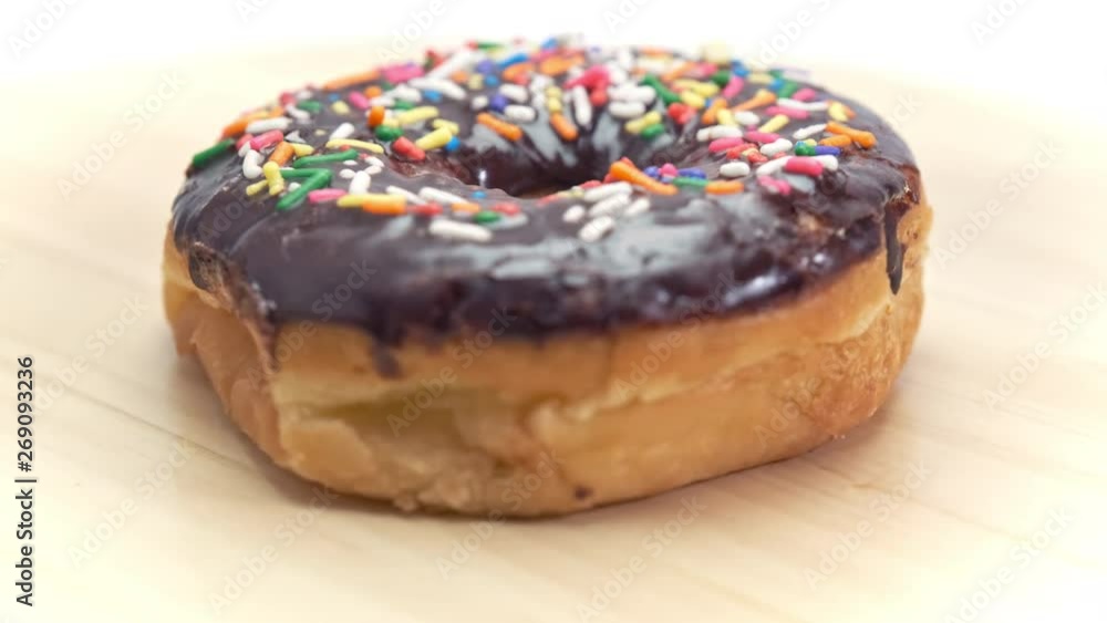 Single Delicious Chocolate-Glazed Donut Turning Slowly on Wood Table Single Delicious Chocolate-Glazed Donut Turning Slowly on Wood Table