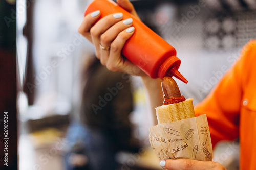 Vinnitsa, Ukraine 10.05.2019: Workflow in Fast Food Cafe: The girl is preparing a French hot dog with ketchup and mustard and sells it to the buyer photo