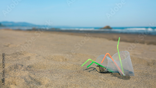 Beach landscape with plastic cups and straws after party