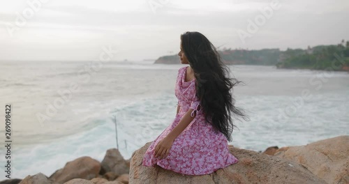 Portrait of a young, South Asian attractive girl sitting on the ocean shore in the evening. The girl dreamily looking at the sunset in slow motion. Shot on Canon 1DX mark2 4K camera photo