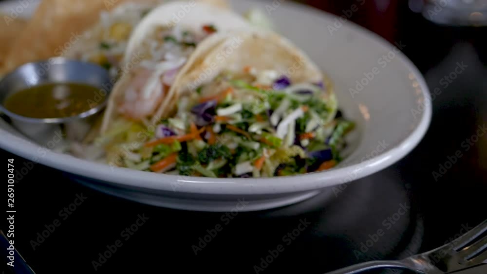 close up on plated fish tacos. The camera moves around a plate of fish tacos with fresh made chips and vegetables. close up on plated fish tacos. The camera moves around a plate of fish tacos with fresh made chips and vegetables.