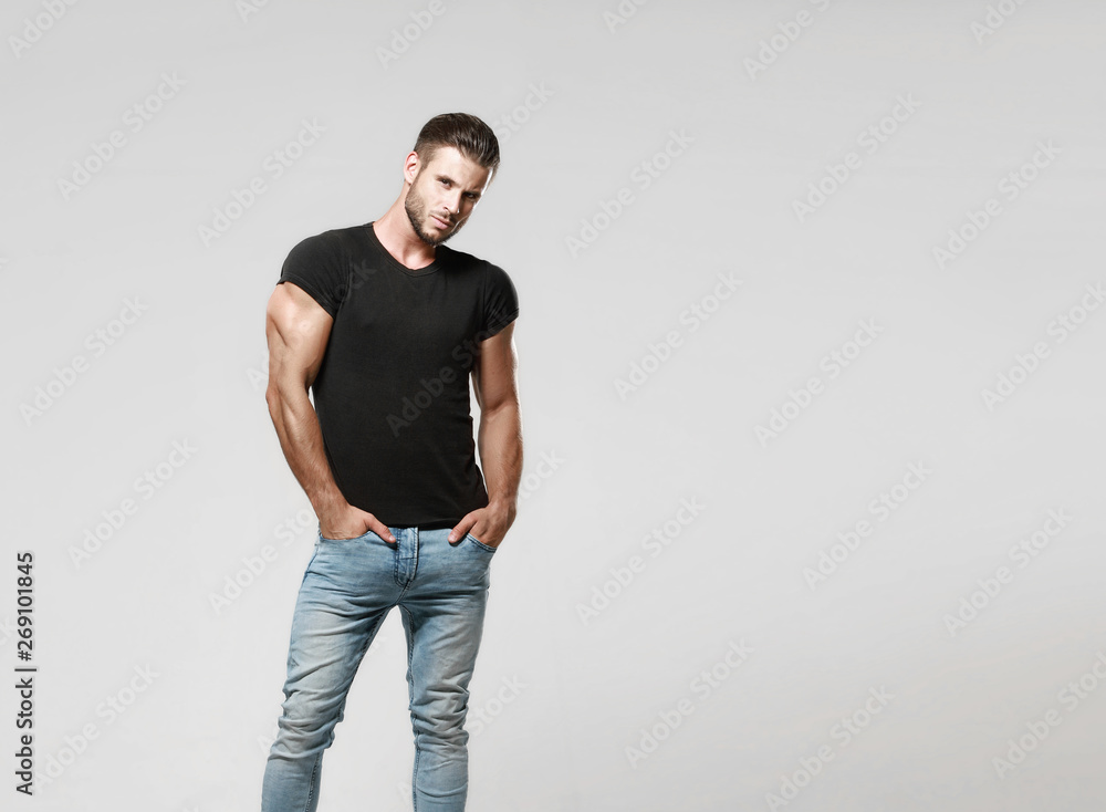 Muscular Model Sports Young Man In Jeans And Black T-Shirt On A Grey  Background. Fashion Portrait Of Brutal Sporty Healthy Strong Muscle Guy  With A Modern Trendy Hairstyle. Stock Photo | Adobe