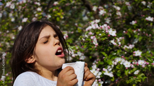 a little pretty girl sneezes into a handkerchief over a spring pollen allergy