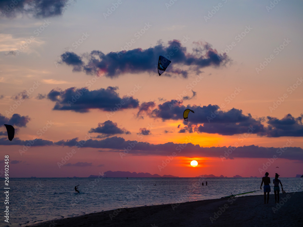 Silhouette of people on the beach and flying kites against the background of the setting sun and clouds of Koh Phangan. Thailand