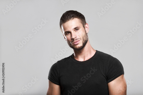 Muscular model young man with beard in black t-shirt on gray background. Fashion portrait of brutal sporty sexy strong muscle guy with modern trendy hairstyle. Model, fashion concept.