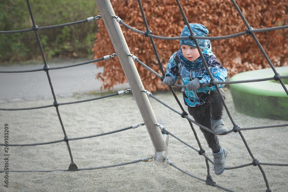 Small boy is climbing the rope ladder at playground in spring Stock Photo