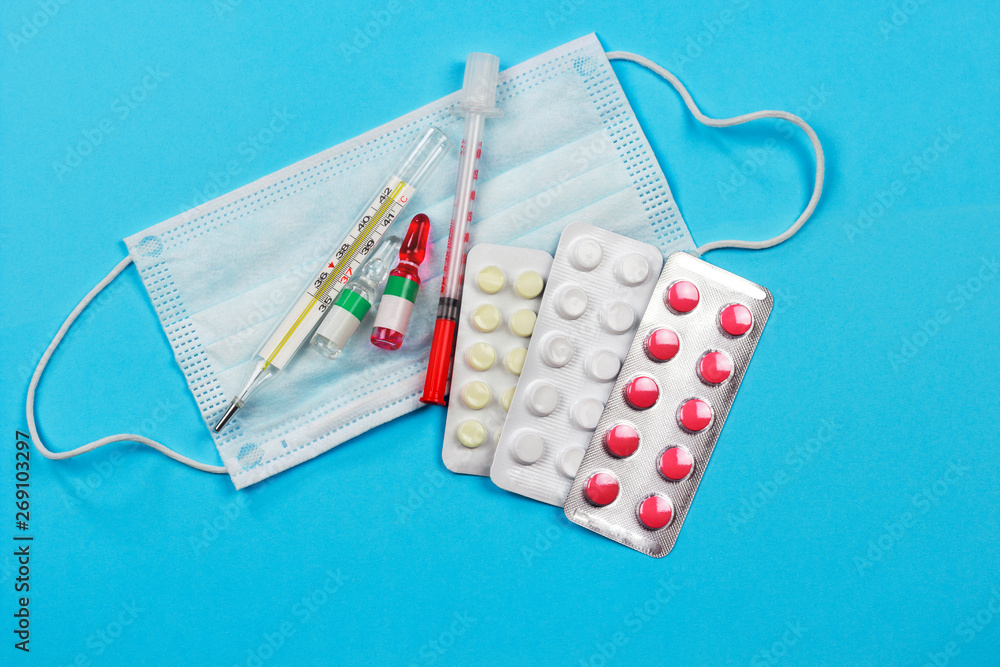 medical protective mask with medicines, syringe and thermometer on a blue background medical protective mask with medicines, syringe and thermometer on a blue background