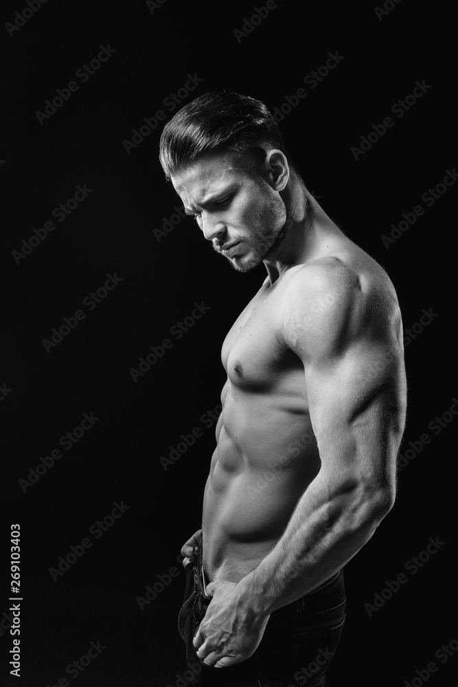 Muscular model young man on dark background. Black and white fashion portrait of strong brutal guy with modern trendy hairstyle. Sexy naked torso six pack abs. Male flexing his muscles. Sport concept. Muscular model young man on dark background. Black and white fashion portrait of strong brutal guy with modern trendy hairstyle. Sexy naked torso six pack abs. Male flexing his muscles. Sport concept.