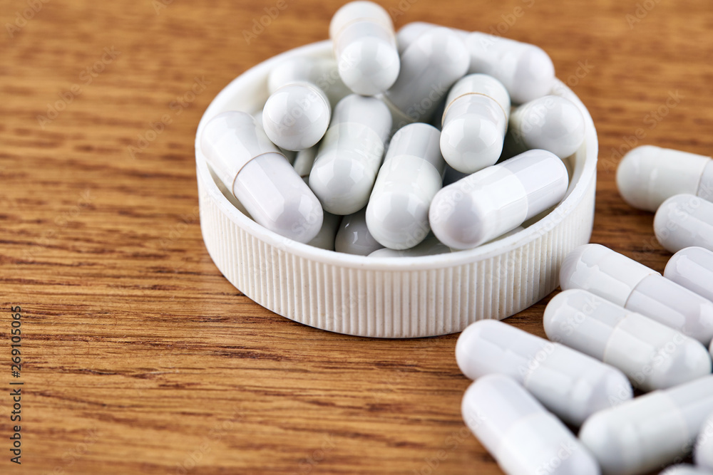 Many white capsules in plastic cap on wooden background