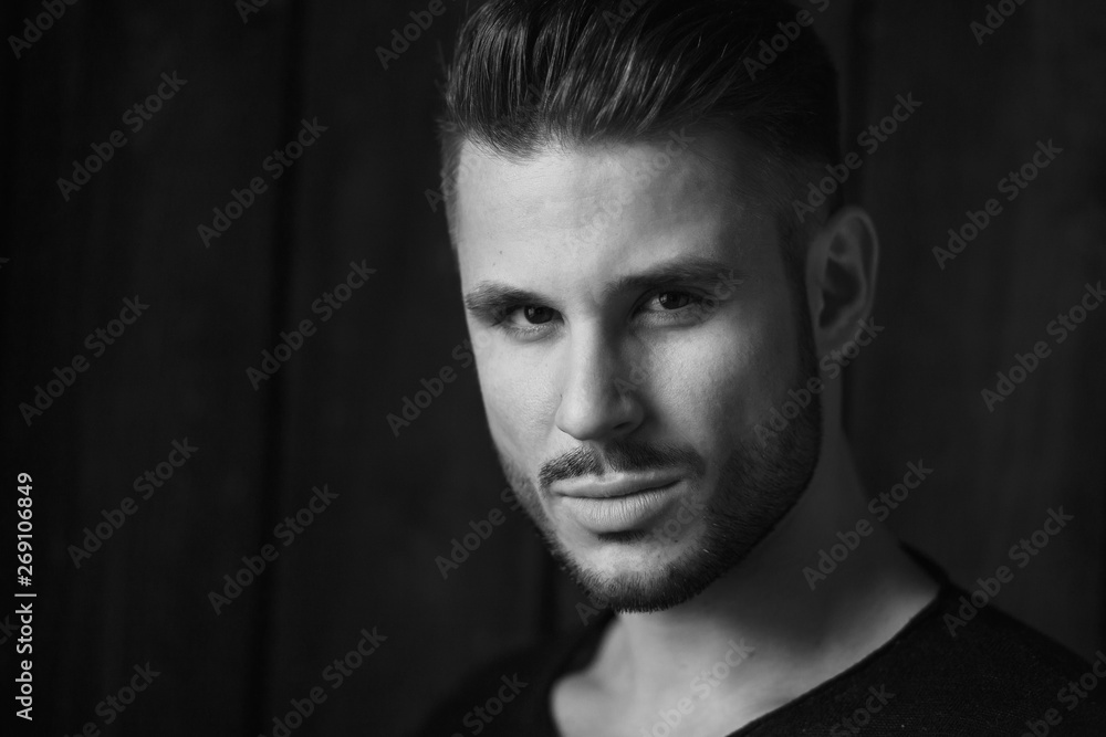 Black and white. Muscular model young man with beard in black t-shirt on dark wooden background. Fashion portrait of brutal sporty sexy strong guy with modern trendy hairstyle. Model, fashion concept.
