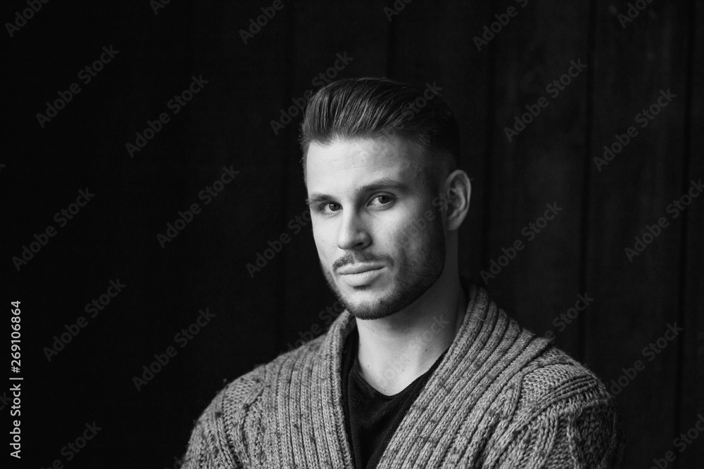 Black and white. Muscular model young man with beard in knitted sweater on dark background. Fashion portrait of brutal sporty sexy strong guy with modern trendy hairstyle. Model, fashion concept. Black and white. Muscular model young man with beard in knitted sweater on dark background. Fashion portrait of brutal sporty sexy strong guy with modern trendy hairstyle. Model, fashion concept.