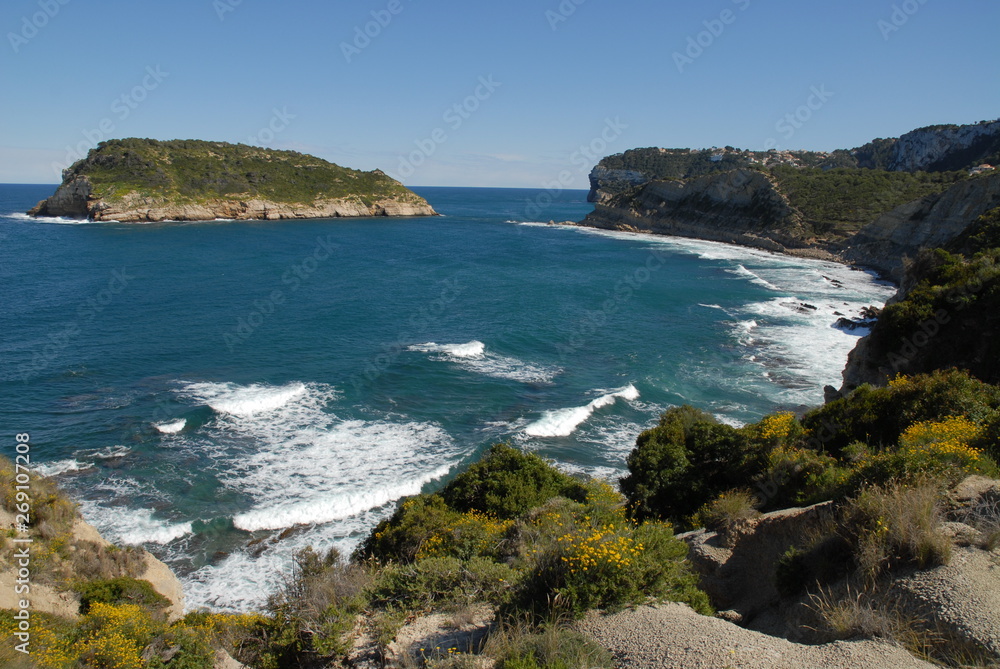 Coastal view with waves breaking on the shoreline in spring,  to the island of Portichol from the headland at Cap Prim, Javea, Alicante Province, Spain