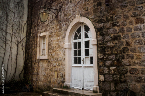 White semicircular door with glass in the stone wall of the old town in Budva, Montenegro © LariBat