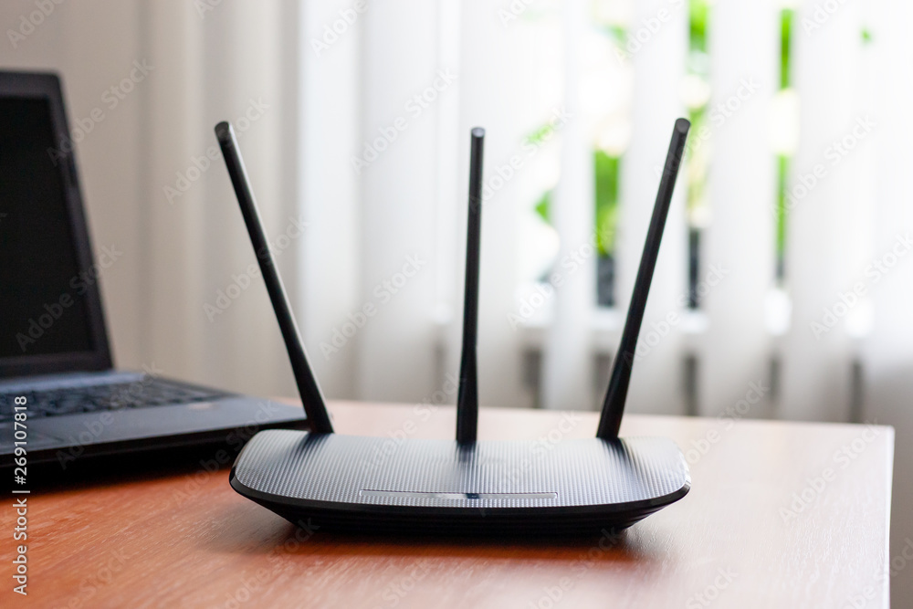 wireless wifi router and laptop at wooden table indoors. window behind.  wireless connection concept. Stock Photo | Adobe Stock