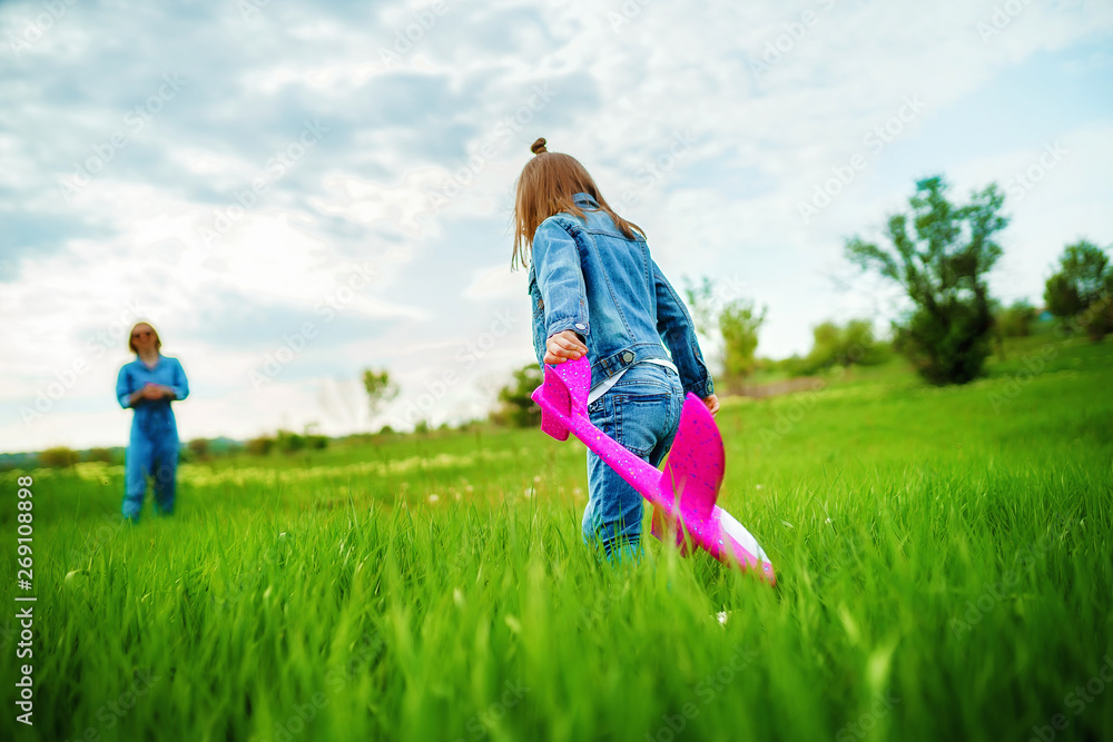 Unrecognizable little girl with pink toy plane walking on green grass towards blurred mother while spending time in countryside together Unrecognizable little girl with pink toy plane walking on green grass towards blurred mother while spending time in countryside together