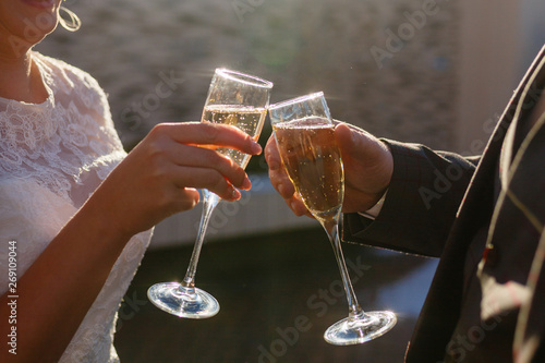 Dating or wedding concept - couple drinking white wine or champagne outdoors. A young couple clink glasses with an alcoholic drink. Sun glare in the glasses. photo