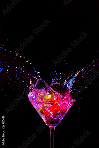 Strawberry in Whine Glass Along With Droplets Colorful Liquid. Isolated Over Black.