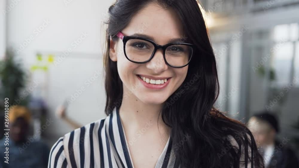 Beautiful young businesswoman fixing hair and smiling on the camera with working group of young business people on the background. Beautiful young businesswoman fixing hair and smiling on the camera with working group of young business people on the background.