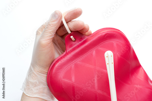 Nurse wearing sterile rubber gloves holds Cleansing Enema Bucket Set on white background. Enema Mug of Esmarch. photo